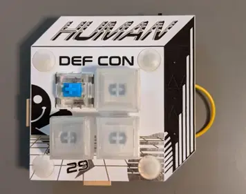 DEF CON 29 conference badge, a cube-shaped board with the word “HUMAN” and three keycaps