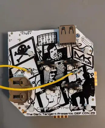 Back of the DEF CON 29 badge with battery holders and a yellow jumper wire